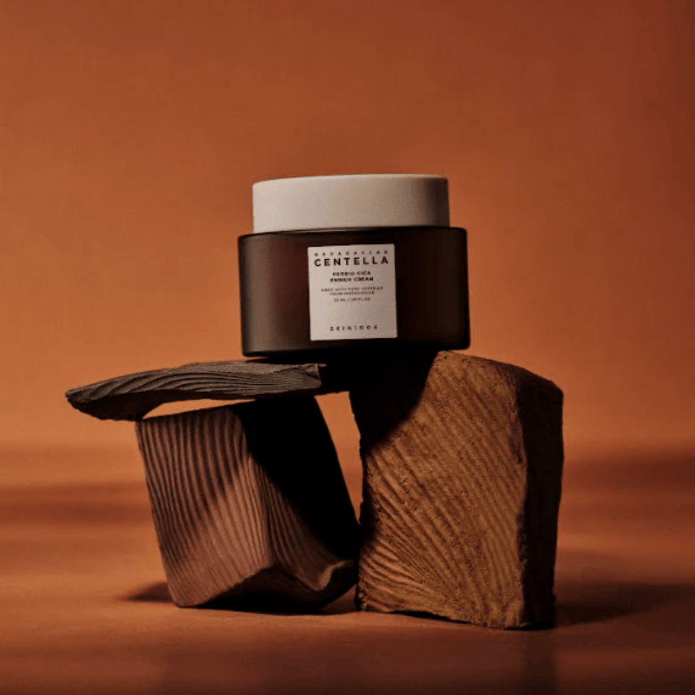 SKIN1004 Madagascar Centella Probio-Cica Enrich Cream σε κομψό καφέ γυάλινο βάζο πάνω σε διακοσμητικά ξύλινα μπλοκ - θρεπτική κορεατική κρέμα προσώπου που ενισχύει το φράγμα του δέρματος.