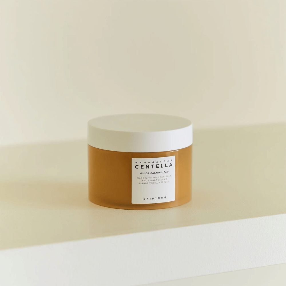 SKIN1004 Madagascar Centella Quick Calming Pad τοποθετημένο σε λευκό ράφι – κεχριμπαρένιο δοχείο με λευκό καπάκι και ευδιάκριτη ετικέτα μπροστά.