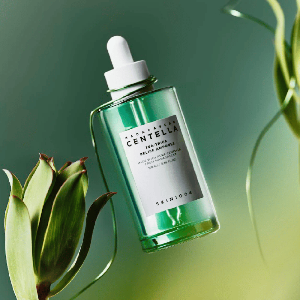 SKIN1004 Madagascar Centella Tea-Trica Relief Ampoule – πράσινο γυάλινο μπουκάλι με πιπέτα, λευκή ετικέτα και περιεχόμενο 100 ml, φωτογραφημένο σε πράσινο φόντο με λεπτομέρειες φυτών.