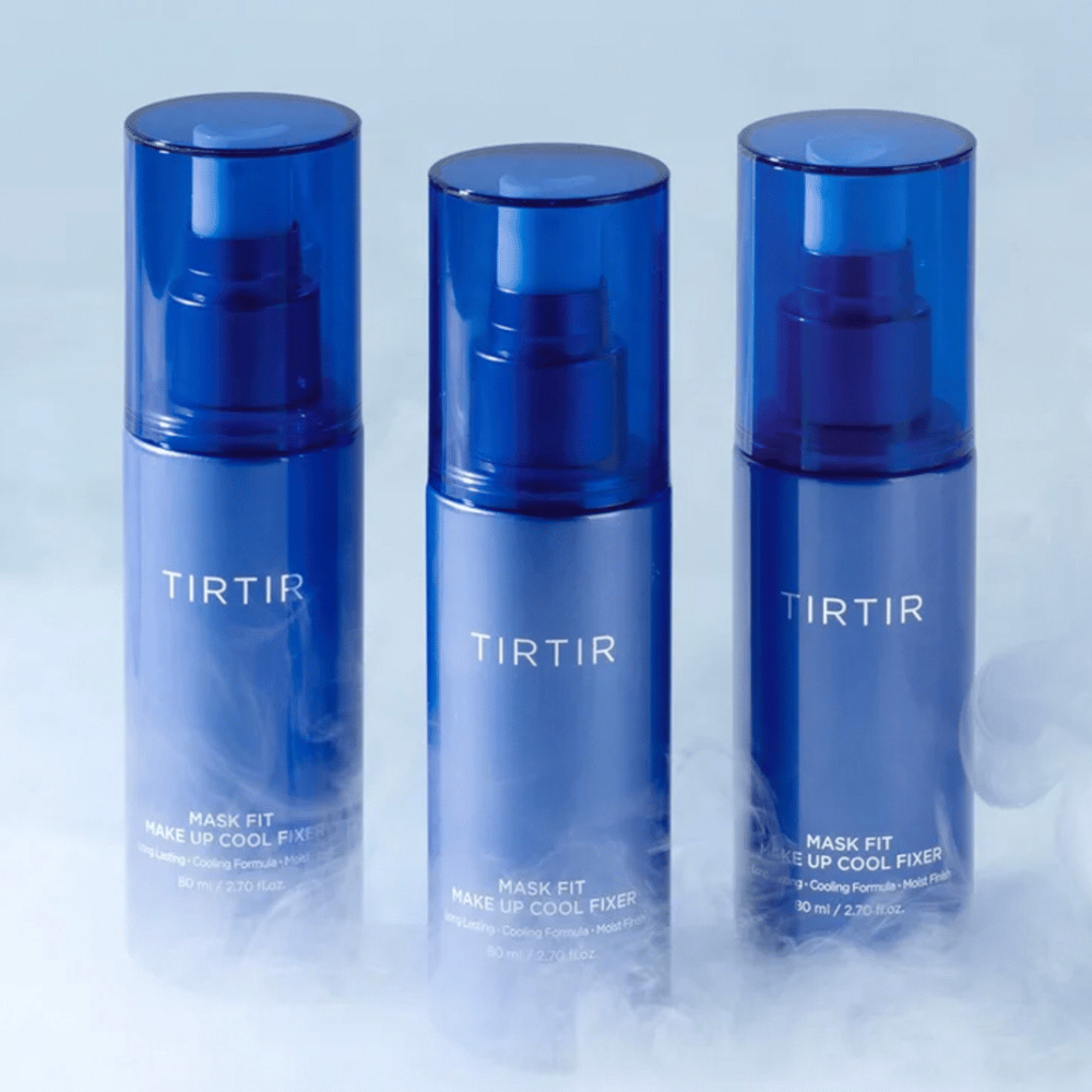 Τρία μπλε μπουκάλια σπρέι με "TIRTIR Mask Fit Make Up Cool Fixer" στην ετικέτα. Κάθε φιάλη χωράει 80 ml (2,70 fl. oz.) και είναι σχεδιασμένη για να προσφέρει μια δροσιστική αίσθηση και μακράς διάρκειας μακιγιάζ. Τα μπουκάλια στέκονται σε ένα φωτεινό υπόβαθρο με ομίχλη για να δημιουργήσουν μια ατμόσφαιρα φρεσκάδας.