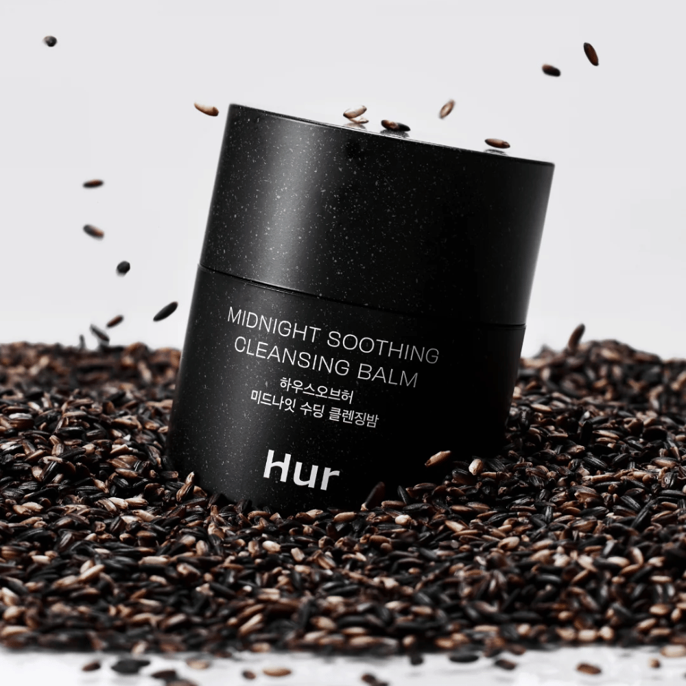 Πώς Midnight Soothing Cleansing Balm σε μαύρο βάζο τοποθετημένο σε μαύρους σπόρους. Καταπραϋντικό καθαριστικό balm που διαλύει το μακιγιάζ και τις ακαθαρσίες ενώ φροντίζει το δέρμα.