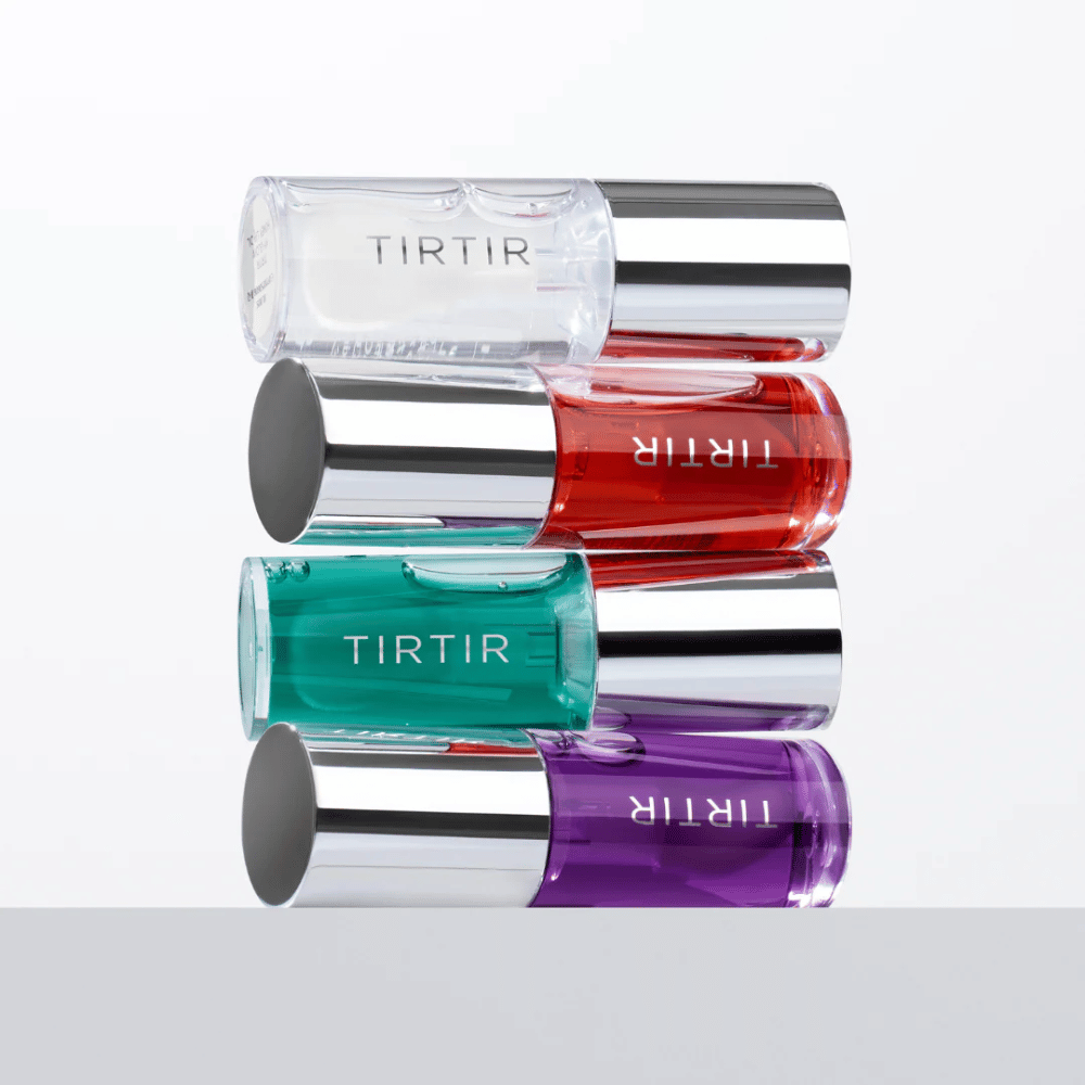 Τέσσερα TIRTIR My Glow Lip Oil σε διάφορα χρώματα – διαφανές, κόκκινο, πράσινο και μοβ – στοιβάζονται το ένα πάνω στο άλλο με ασημένια καπάκια σε λευκό φόντο.