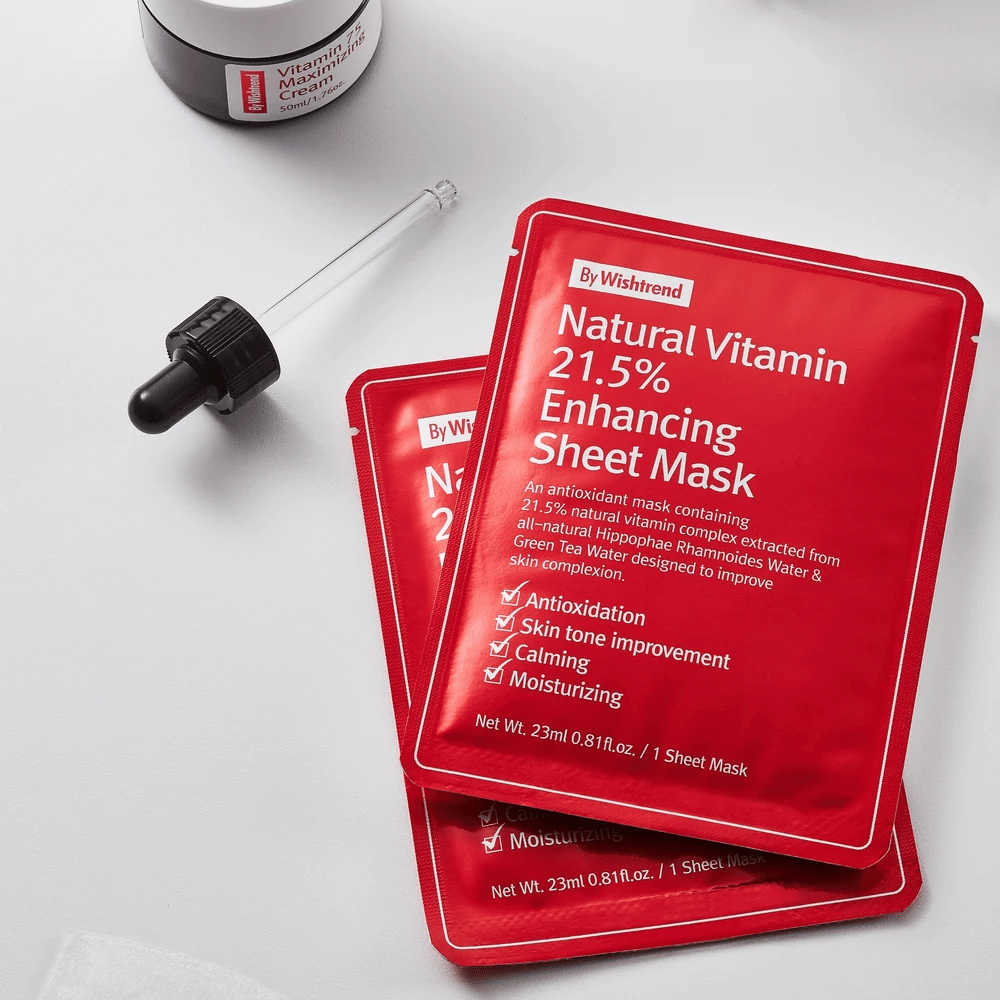 By Wishtrend Natural Vitamin 21.5% Enhancing Sheet Mask σε κόκκινες συσκευασίες, τοποθετημένες σε λευκή επιφάνεια μαζί με μια πιπέτα και ένα βάζο κρέμας προσώπου.
