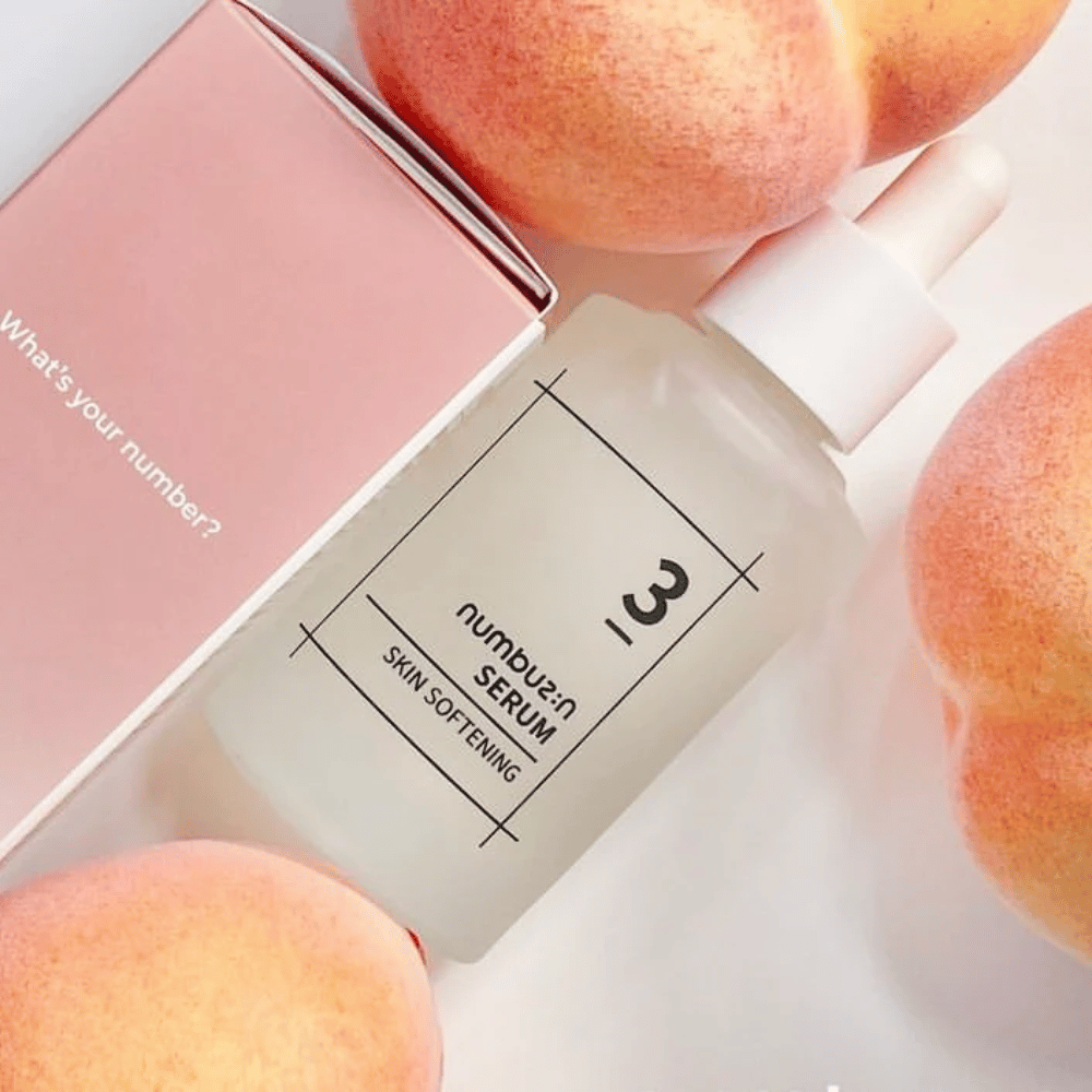 Μπουκάλι με numbus:in No.3 Skin Softening Serum περιτριγυρισμένο από ροδάκινα και ένα ροζ κουτί με το κείμενο "What's your number?".