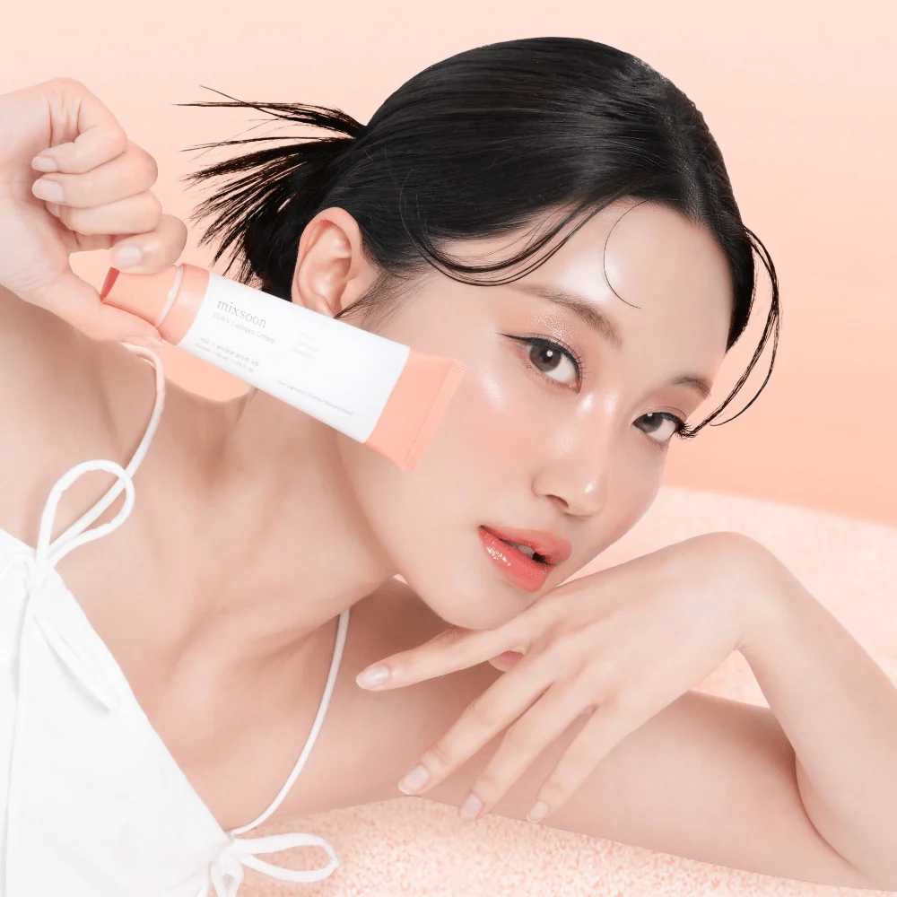 Άτομο με λαμπερό δέρμα κρατάει Mixsoon PDRN Collagen Cream κοντά στο μάγουλο. Η κρέμα ενυδατώνει, ενισχύει την ελαστικότητα και προσφέρει μια φρέσκια λάμψη.
