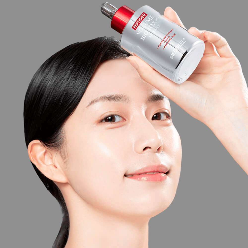 Άτομο κρατάει το MEDI-PEEL Peptide 9 Volume Bio Tox Pro Ampoule στο μέτωπο. Το δέρμα φαίνεται ενυδατωμένο και λαμπερό - ο ορός ενισχύει την ελαστικότητα και τη σφριγηλότητα.