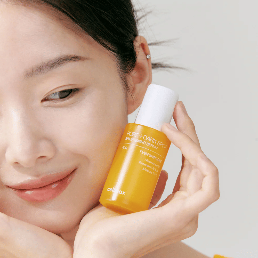 Το μοντέλο κρατάει Celimax Pore + Dark Spot Brightening Serum κοντά στο πρόσωπο, δείχνοντας λαμπερή επιδερμίδα.