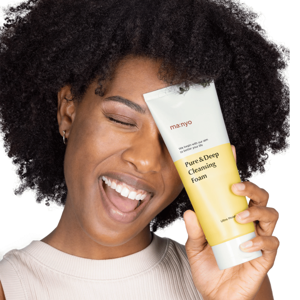 Γυναίκα με σγουρά μαλλιά κρατάει Ma:nyo Pure & Deep Cleansing Foam – ένας απαλός κορεατικός καθαρισμός που αφαιρεί αποτελεσματικά τη βρωμιά και το μακιγιάζ χωρίς να ξηραίνει το δέρμα.