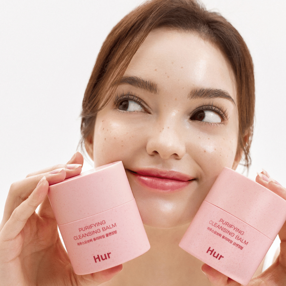 Μοντέλο κρατά δύο βάζα Πώς Purifying Cleansing Balm. Ήπιο καθαριστικό balm που είναι κατάλληλο για ευαίσθητο δέρμα και προσφέρει φρέσκια, ενυδατωμένη αίσθηση μετά τον καθαρισμό.