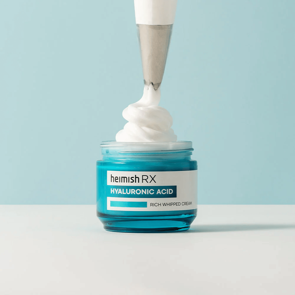 Heimish RX Hyaluronic Acid Rich Whipped Cream σε ένα μπλε γυάλινο βάζο, όπου μια σακούλα ψεκασμού εφαρμόζει την αφράτη κρέμα. Μια ενυδατική κρέμα προσώπου με υαλουρονικό οξύ για εντατική ενυδάτωση και απαλή, γεμάτη επιδερμίδα.