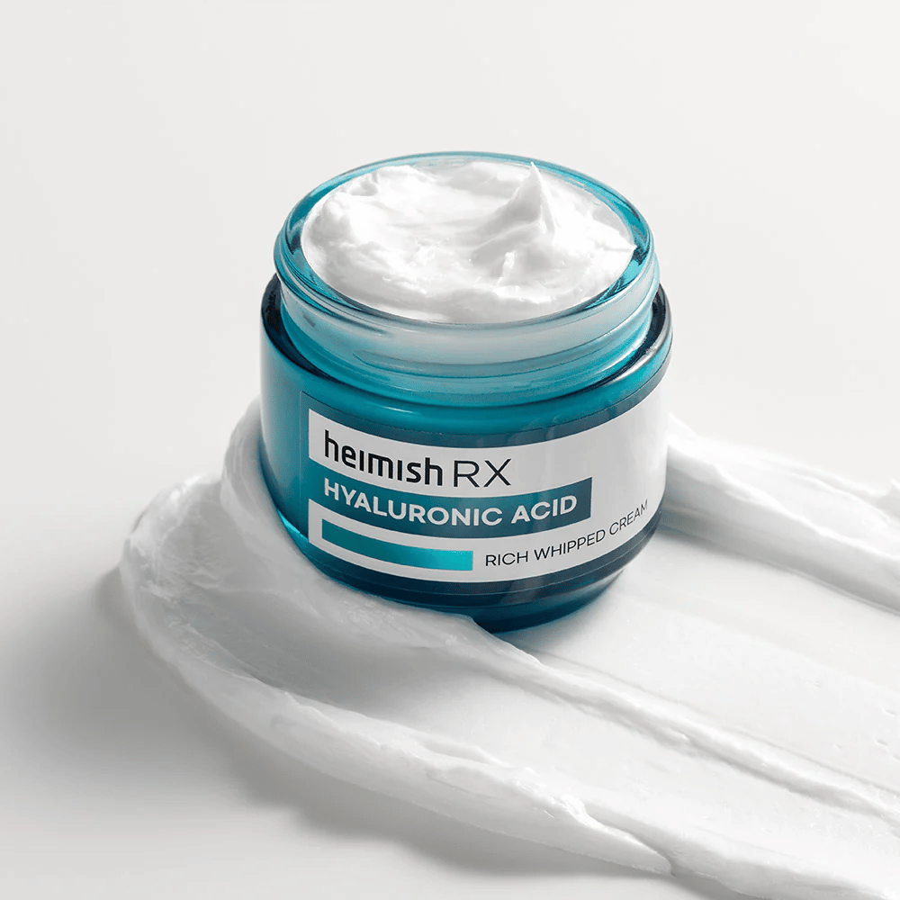Heimish RX Hyaluronic Acid Rich Whipped Cream σε ένα μπλε γυάλινο βάζο με πλούσια και αφράτη υφή, απλωμένη σε λευκό φόντο. Εντατικά ενυδατική κρέμα προσώπου με υαλουρονικό οξύ για βαθιά ενυδάτωση και απαλή επιδερμίδα.