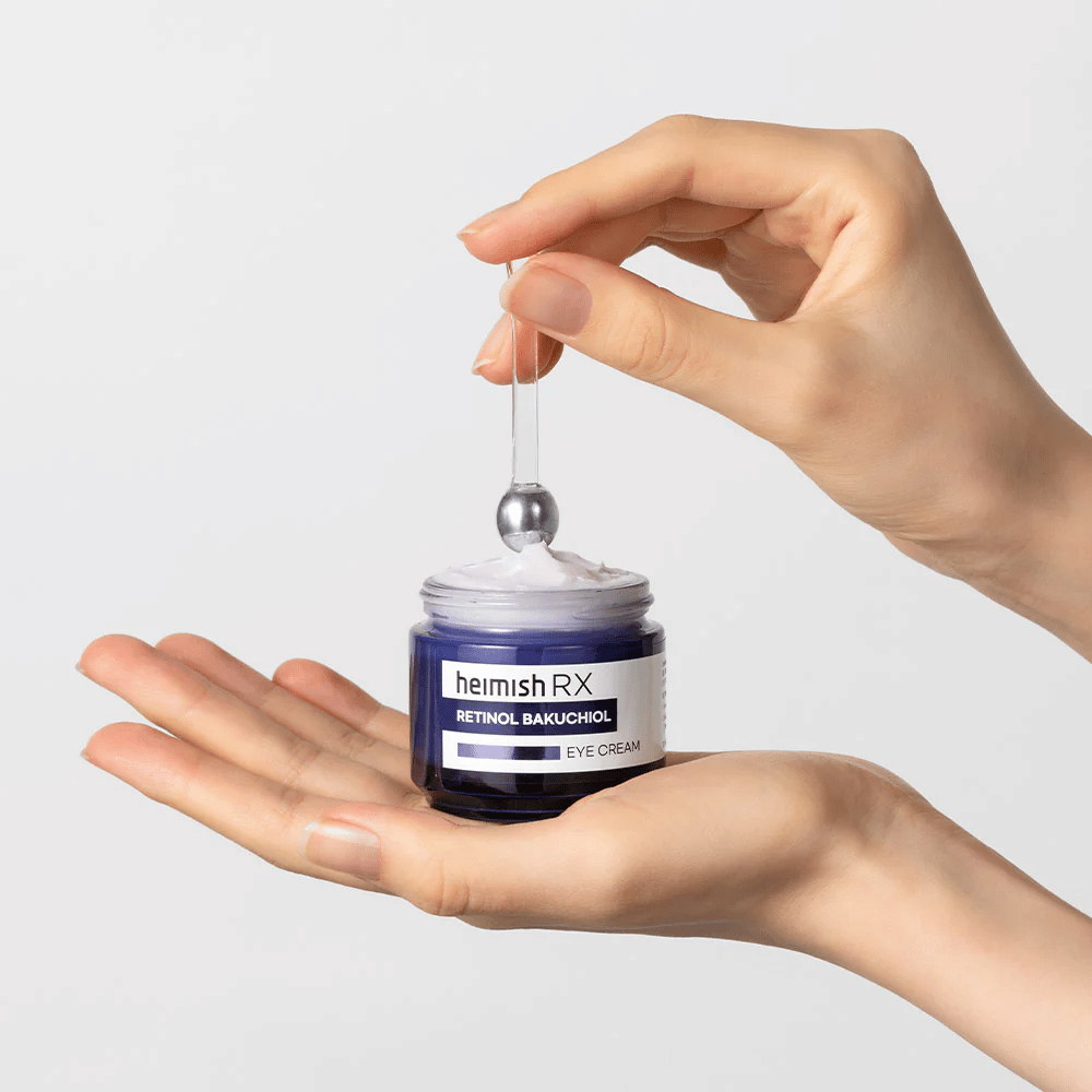 Heimish RX Retinol Bakuchiol Eye Cream σε ένα κομψό μπλε δοχείο, ανασηκωμένο με μεταλλικό απλικατέρ. Μια κρέμα ματιών με ρετινόλη και μπακουχιόλη για τη μείωση των λεπτών γραμμών και για πιο σφριγηλή επιδερμίδα.
