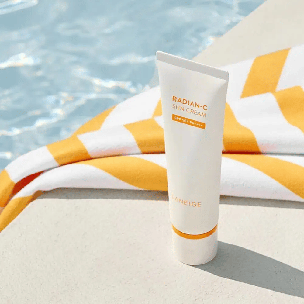 LANEIGE Radian-C Sun Cream στέκεται δίπλα στην άκρη της πισίνας με μια πετσέτα με κίτρινες και λευκές ρίγες στο φόντο.