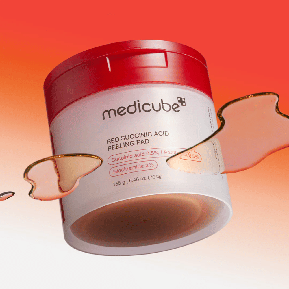 Medicube Red Succinic Acid Peeling Pad σε ένα λευκό και κόκκινο δοχείο, τοποθετημένο σε ένα φόντο με διαβάθμιση σε κόκκινο και πορτοκαλί. Το προϊόν περιέχει σουκινικό οξύ και νιασιναμίδη για απολέπιση και βελτίωση του δέρματος. Υγρή υφή φαίνεται γύρω από το δοχείο.