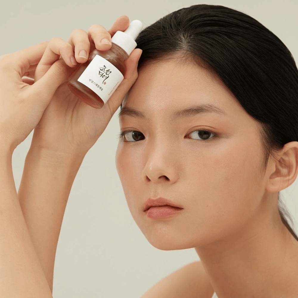 Μοντέλο κρατάει Beauty of Joseon Revive Serum στο μάγουλο – θρεπτικός ορός με ginseng και βλέννα σαλιγκαριού.