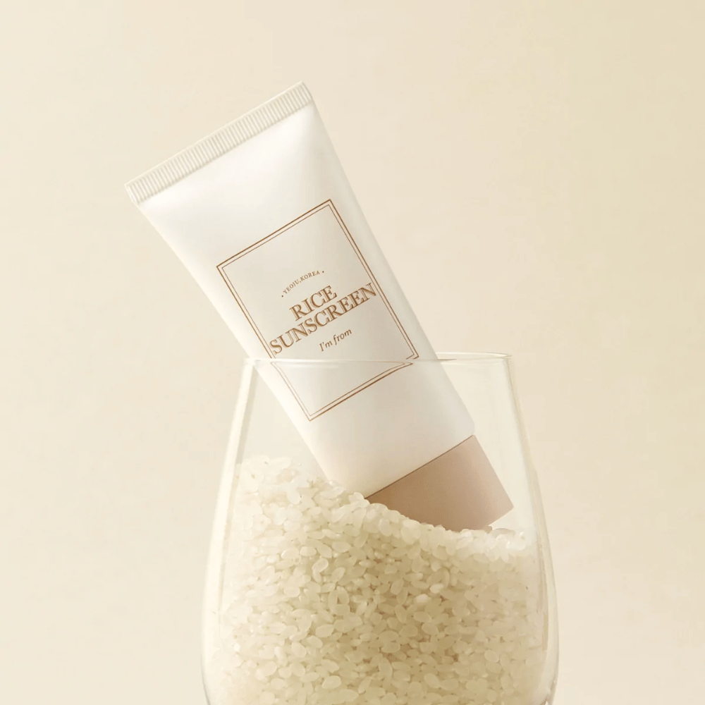 Σωλήνας με "I'm from" Rice Sunscreen, SPF50+ PA++++, τοποθετημένος σε ένα ποτήρι με κόκκους ρυζιού.