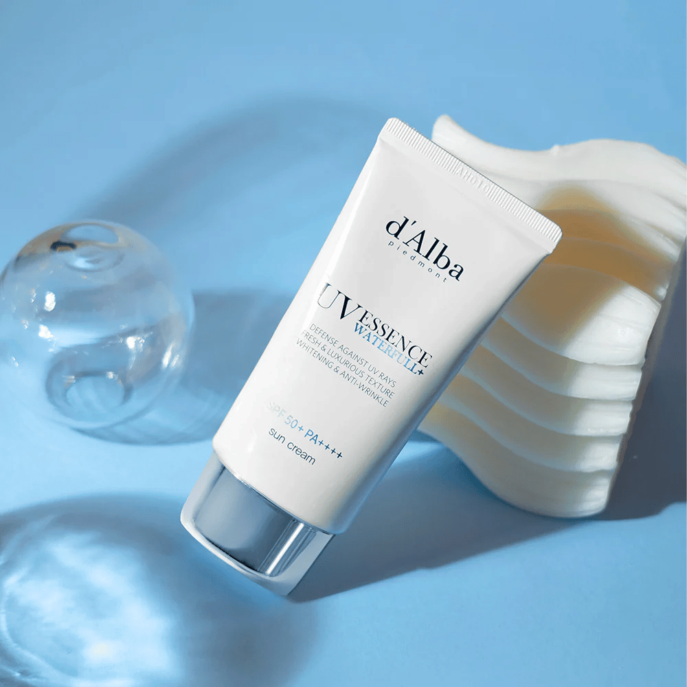 d'Alba UV Essence Waterfull+ Sun Cream με SPF 50+ PA++++ βρίσκεται σε μπλε φόντο με αντανακλάσεις φωτός και διακοσμητικά στοιχεία – τονίζει τις φρέσκες και ενυδατικές ιδιότητες της αντηλιακής κρέμας.