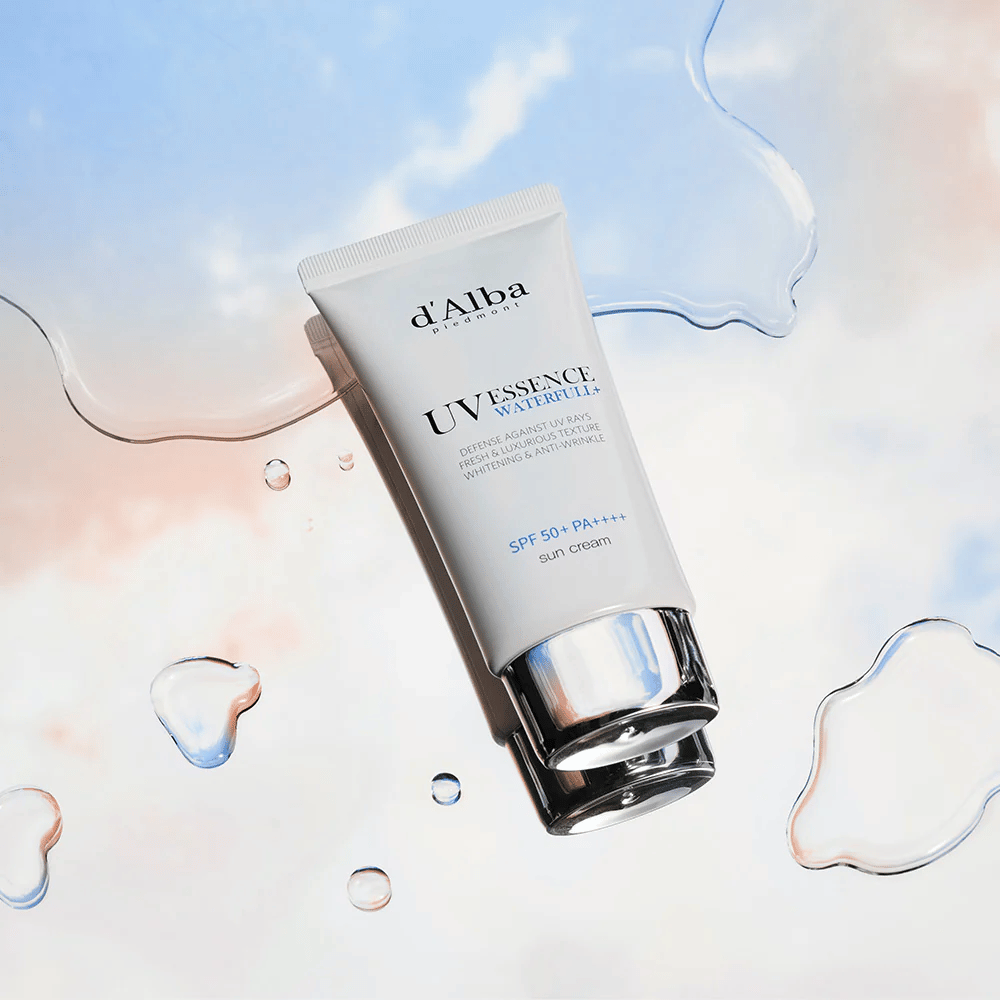 Εικόνα προϊόντος της d'Alba UV Essence Waterfull+ Sun Cream με SPF 50+ PA++++, τοποθετημένη σε φόντο με πιτσιλιές νερού και μπλε-ροζ ουρανό – συμβολίζει την ελαφριά και ενυδατική αντηλιακή προστασία.