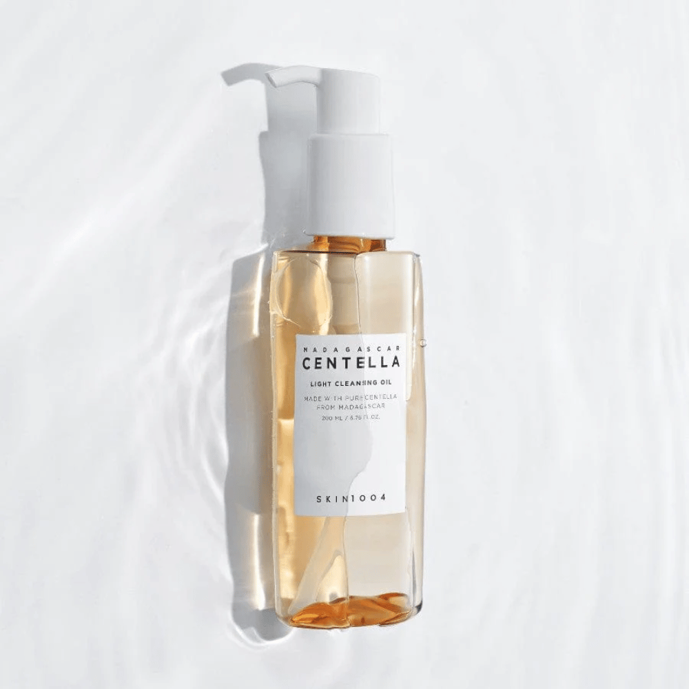 SKIN1004 Madagascar Centella Light Cleansing Oil σε λευκό φόντο με απαλές αντανακλάσεις του νερού που αναδεικνύουν το διαφανές μπουκάλι και το χρυσό περιεχόμενο.