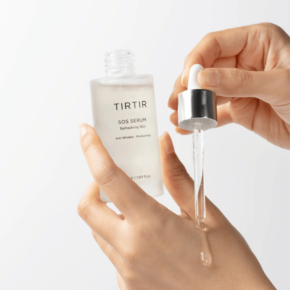 Χέρια που στάζουν TIRTIR SOS Serum από μια πιπέτα, σχεδιασμένο για φροντίδα δέρματος.