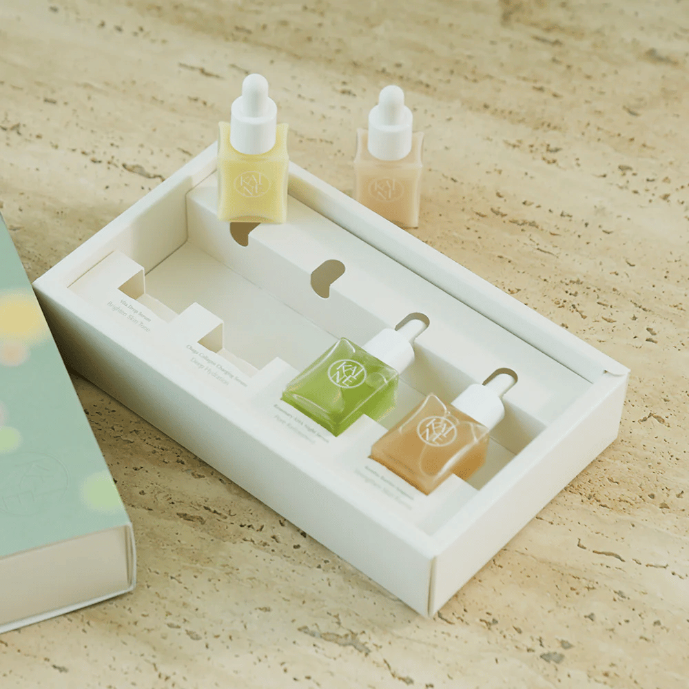 Τέσσερα πολύχρωμα μπουκάλια ορού από KAINE Serum Discovery Kit με καπάκι πιπέτας, σχεδιασμένα για να καλύπτουν διάφορες ανάγκες του δέρματος σε μια μινιμαλιστική και κομψή συσκευασία.