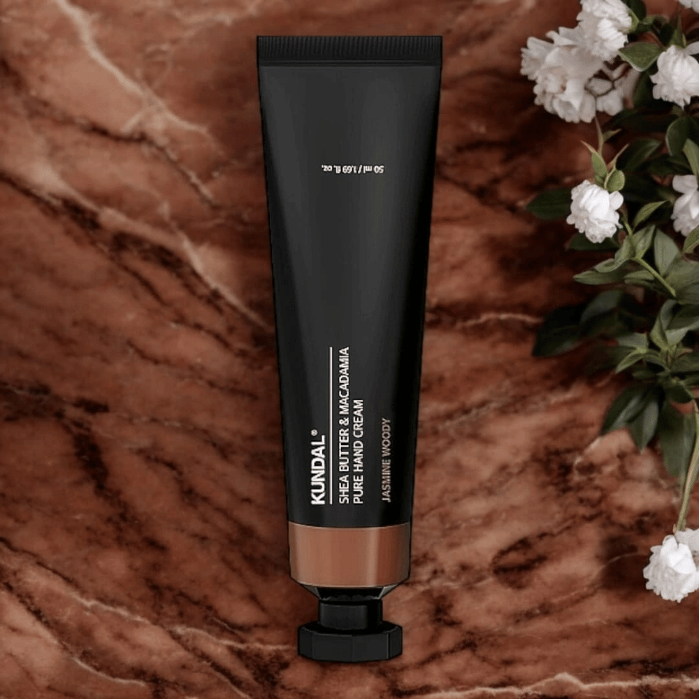KUNDAL Shea Butter & Macadamia Pure Hand Cream Jasmine Woody τοποθετημένη σε μάρμαρο με λουλούδια – θρεπτική κρέμα χεριών που φροντίζει τα ξηρά χέρια και προσφέρει ένα κομψό άρωμα jasmine woody.
