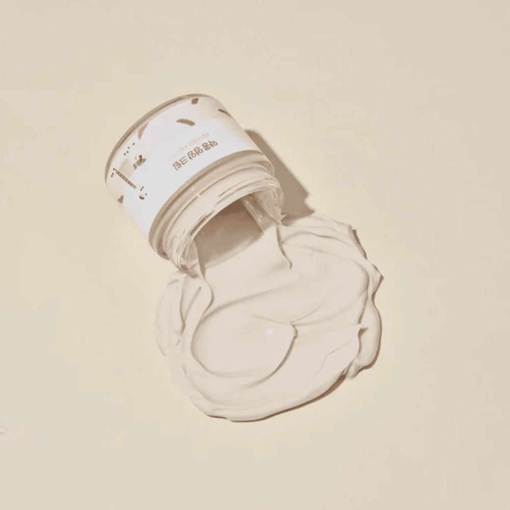 Mixsoon Soybean Nourishing Cream spilld ur burken på en beige bakgrund. Krämens fylliga konsistens visar dess intensiva återfuktande egenskaper.