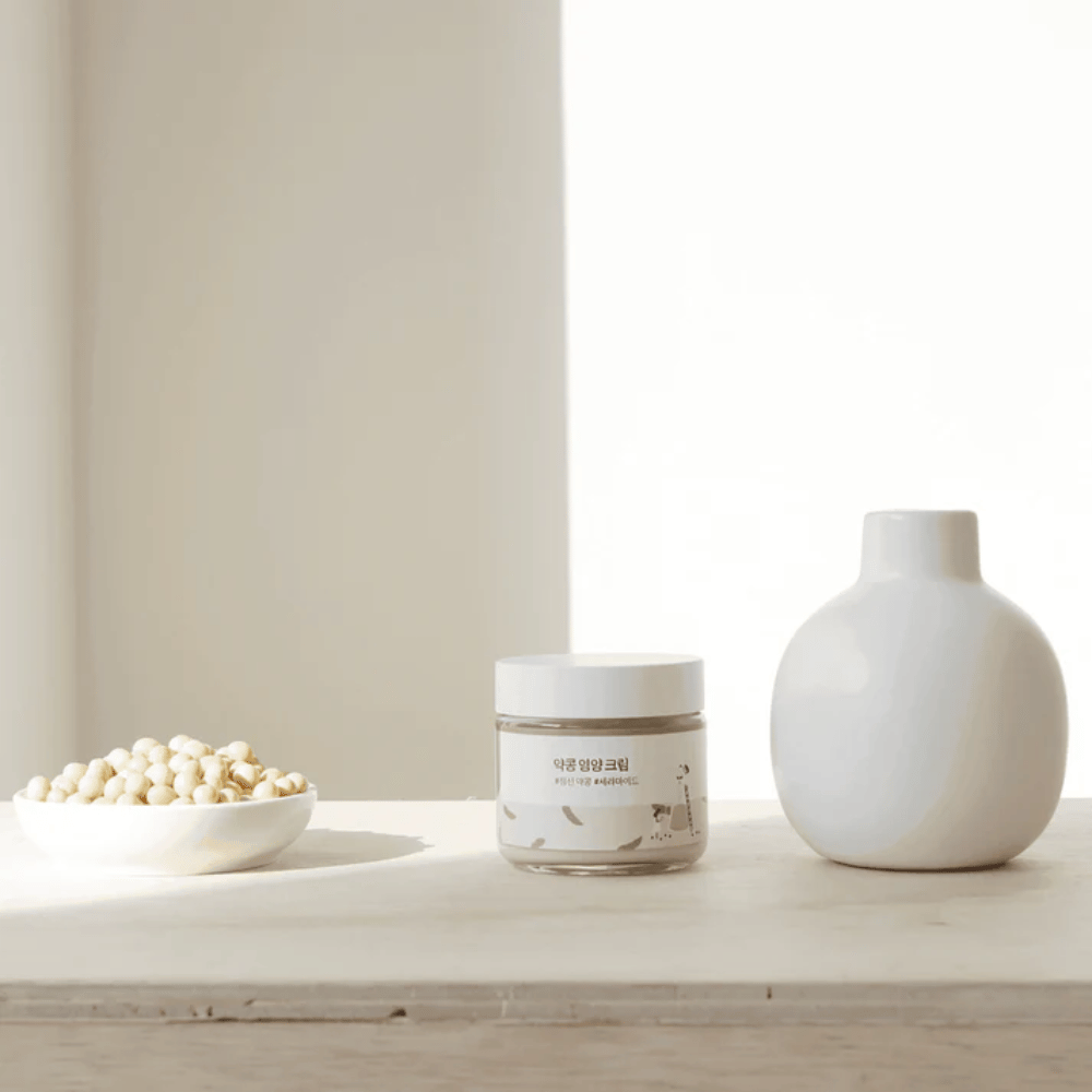 Mixsoon Soybean Nourishing Cream στέκεται σε ένα ξύλινο τραπέζι δίπλα σε ένα βάζο και φασόλια σόγιας. Μια μινιμαλιστική, ενυδατική κρέμα με φυσικά συστατικά.