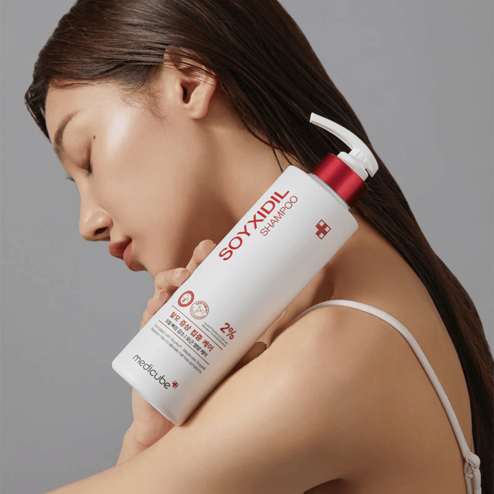 Kvinna med långt hår lutar huvudet mot en flaska Medicube Soyxidil Shampoo, som stärker hårbotten och motverkar håravfall.