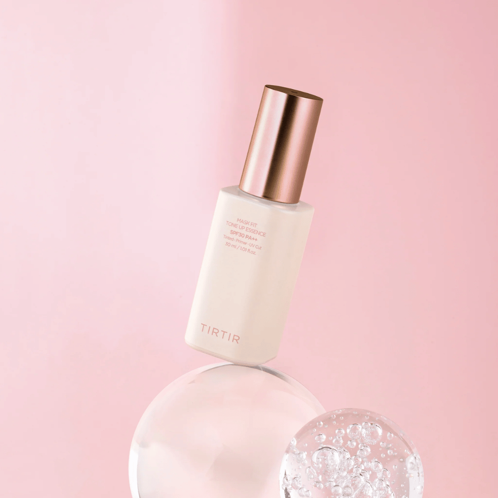 Η εικόνα δείχνει ένα μπουκάλι "TIRTIR MASK FIT TONE UP ESSENCE" με SPF30 PA++ σε ροζ φόντο, που δίνει μια αίσθηση απαλότητας και θηλυκότητας.
