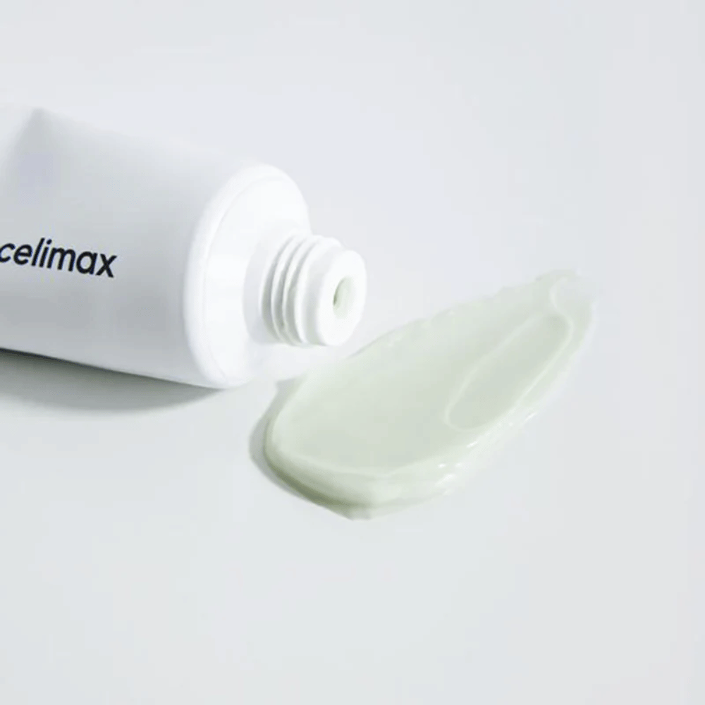 Celimax Noni Energy Repair Cream σε λευκό σωληνάριο με μια μικρή ποσότητα ανοιχτοπράσινης κρέμας απλωμένη δίπλα στο σωληνάριο σε λευκή επιφάνεια. Η κρέμα είναι για θρέψη και επισκευή του δέρματος.