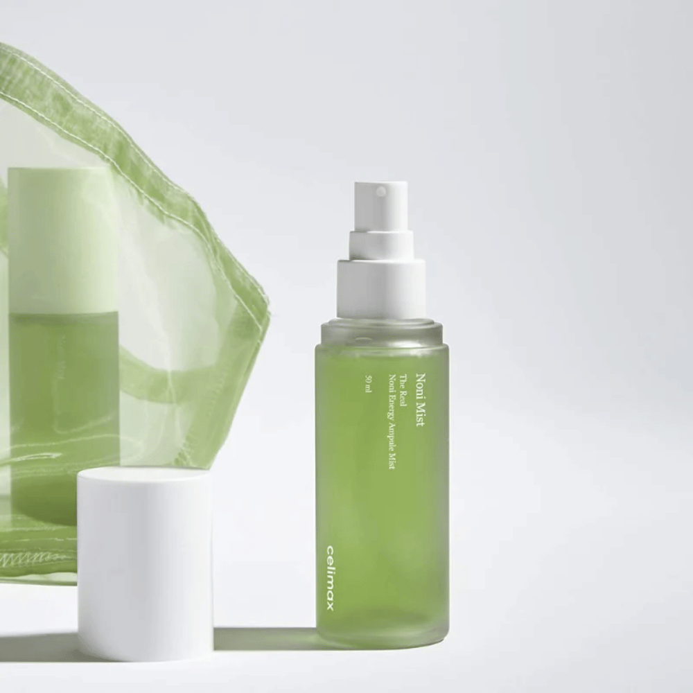 Ένα μπουκάλι με Celimax Noni Mist, ένα πράσινο μπουκάλι με λευκή αντλία, που στέκεται δίπλα σε ένα καπάκι. Το προϊόν είναι συσκευασμένο σε μια διαφανή πλαστική σακούλα και προωθείται ως Noni Energy Ampule Mist.