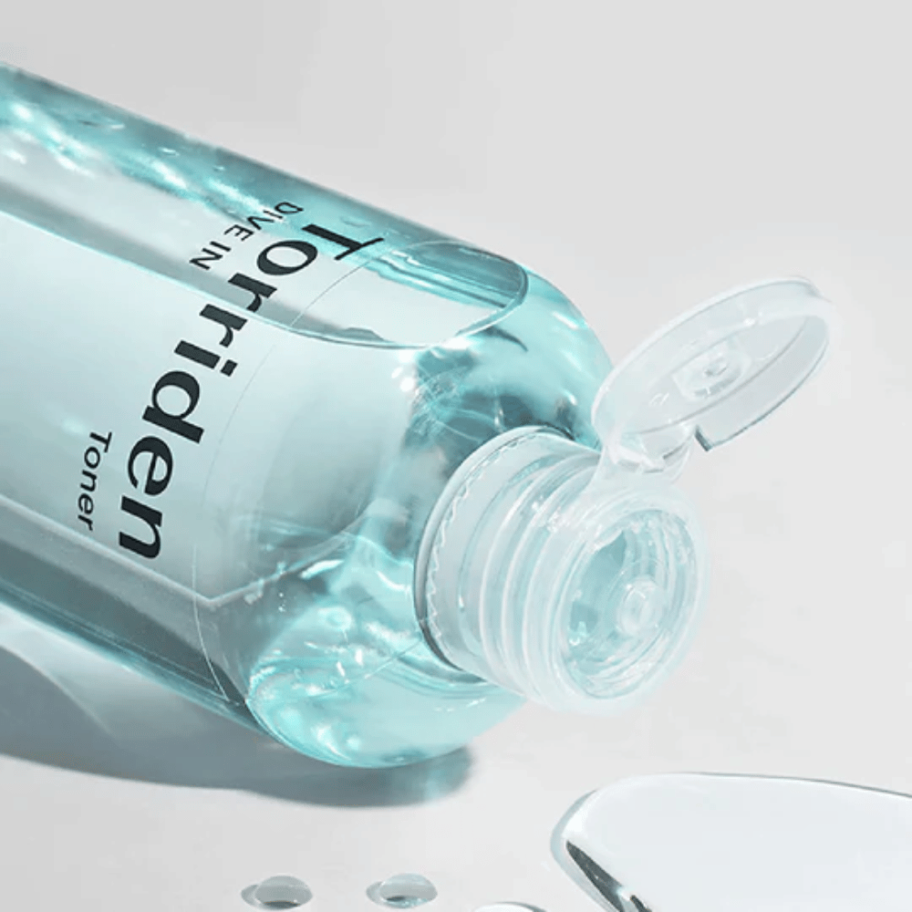 Ένα μπουκάλι DIVE-IN Low Molecule Hyaluronic Acid Toner 300ml δίπλα σε ένα ποτήρι νερό, προάγει Torriden και ενυδάτωση.