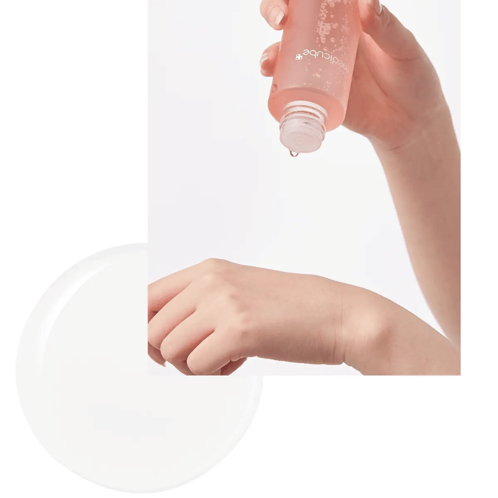 Χέρι που ρίχνει το Medicube Triple Collagen Toner 4.0 από ένα ροζ μπουκάλι στο δέρμα, δείχνοντας την ενυδατική υφή.
