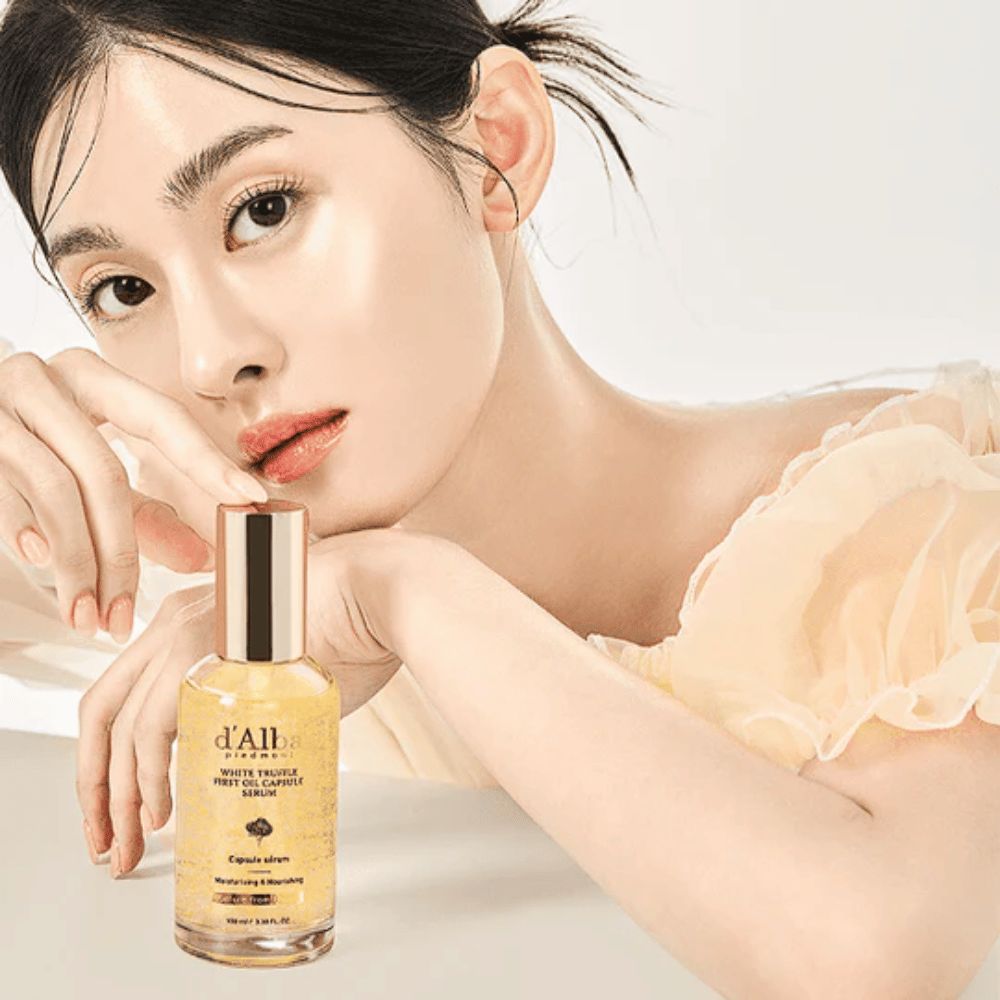 Modell med glödande hud poserar bredvid d'Alba White Truffle First Oil Capsule Serum.