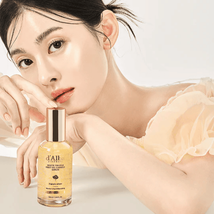 Modell med glödande hud poserar bredvid d'Alba White Truffle First Oil Capsule Serum.