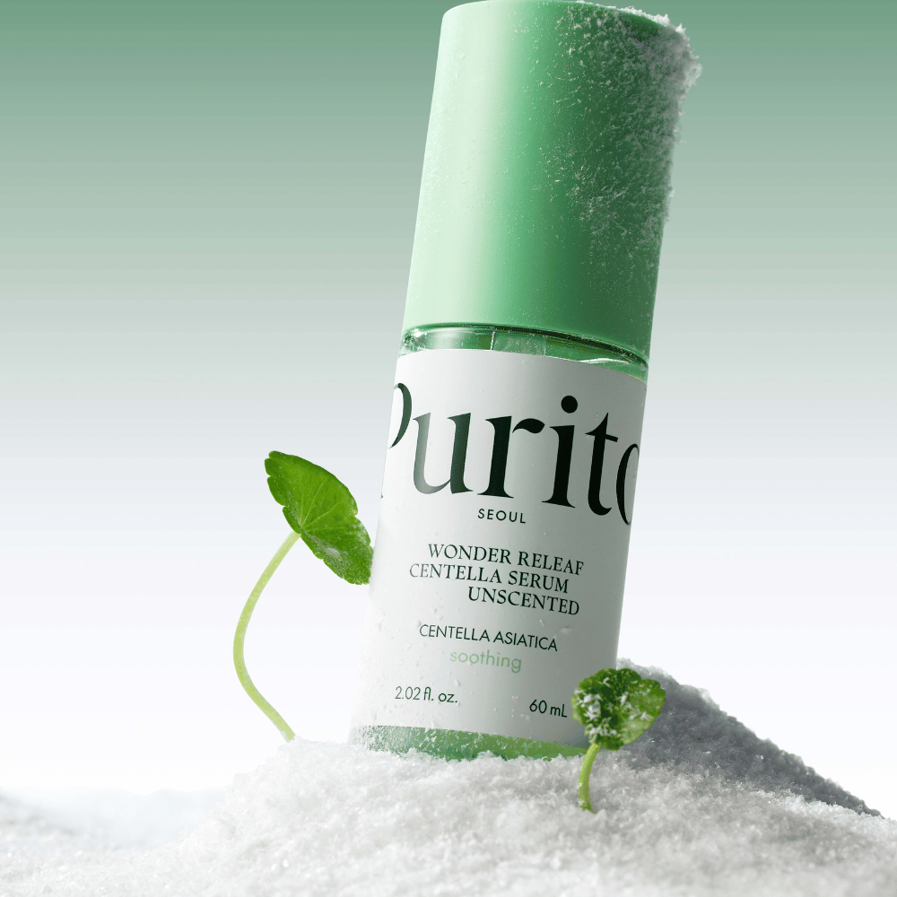 Μπουκάλι με Purito Centella Serum βρίσκεται στο χιόνι, φαίνονται πράσινα φύλλα, σε μαλακό πράσινο φόντο.