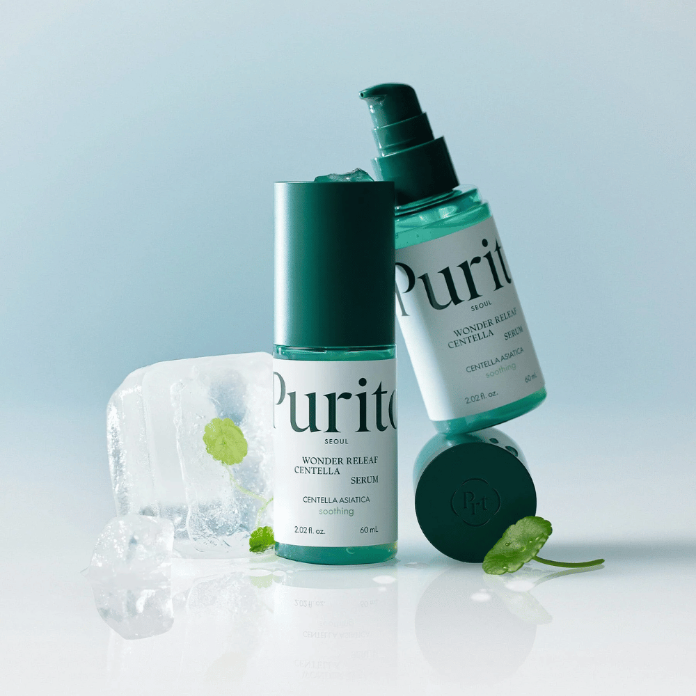 Δύο μπουκάλια από Purito Wonder Releaf Centella Serum, το ένα όρθιο και το άλλο ξαπλωμένο, περιτριγυρισμένα από κομμάτια πάγου με φύλλα centella μέσα και ένα χαλαρό φύλλο σε ανοιχτό μπλε επιφάνεια.