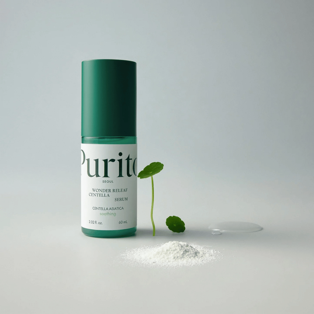 Πράσινο μπουκάλι από Purito Wonder Releaf Centella Serum 60 ml στέκεται σε λευκή επιφάνεια, περιτριγυρισμένο από φύλλα centella, μία διαφανή σταγόνα ορού και μία μικρή λευκή σκόνη.