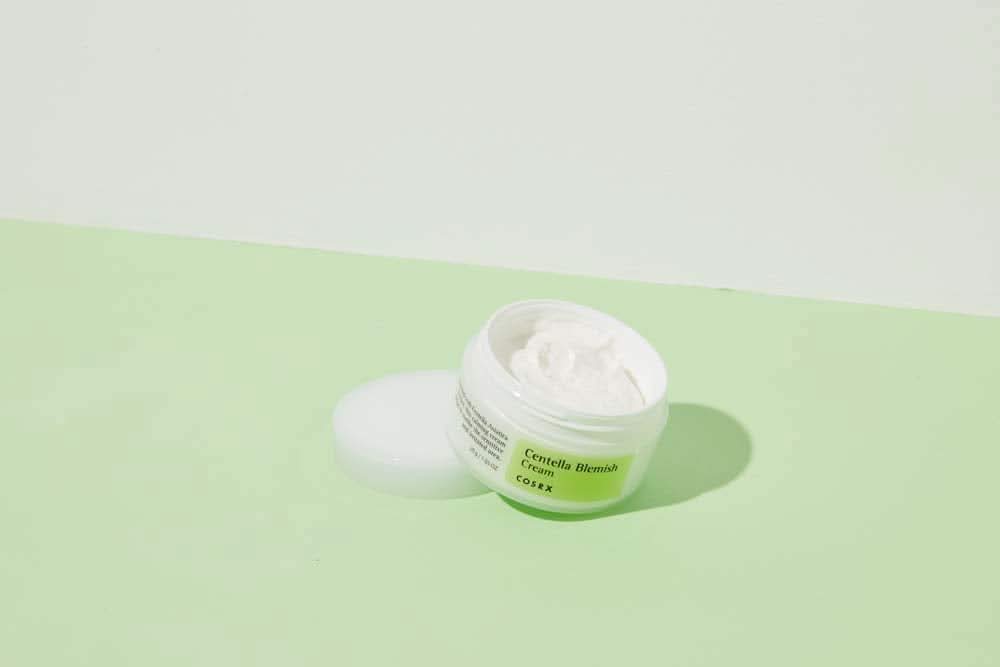 Ένα βαζάκι COSRX Centella Blemish Cream 30ml που βρίσκεται σε μια πράσινη επιφάνεια.