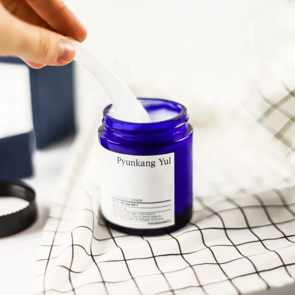 Ένα άτομο χρησιμοποιεί ένα δοχείο Pyunkang Yul Nutrition Cream 100ml σε ένα τραπέζι.