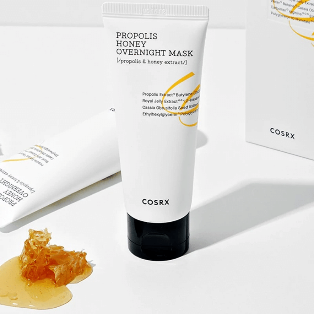 Ένα κουτί Full Fit Propolis Honey Overnight Mask 60ml από COSRX με ένα μπουκάλι μέλι δίπλα, με εκχύλισμα πρόπολης.