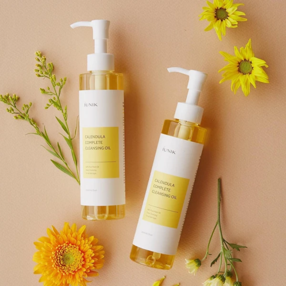 Δύο μπουκάλια iUNIK Calendula Complete Cleansing Oil 200ml με κίτρινα λουλούδια σε μπεζ φόντο, εμποτισμένα με φυτικό έλαιο.