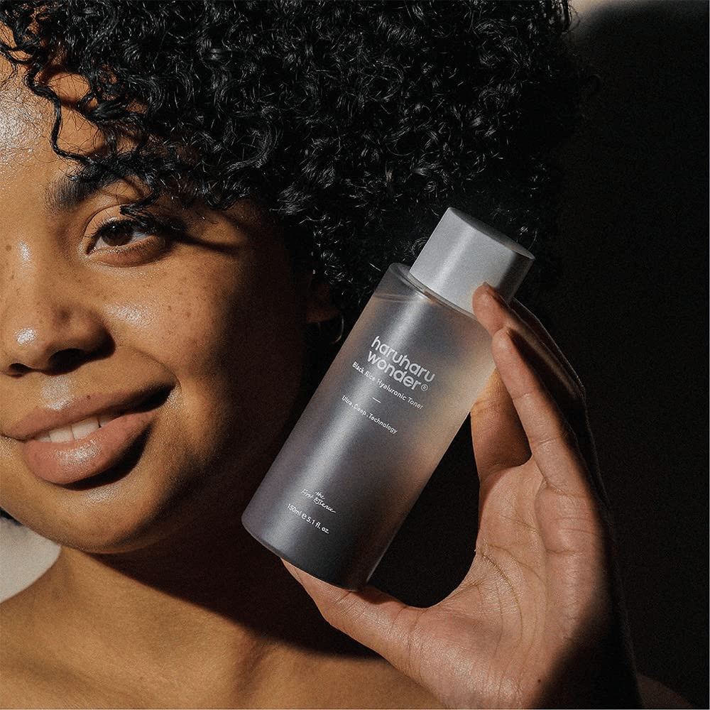 Μια γυναίκα που κρατάει ένα μπουκάλι Haruharu Wonder Black Rice Hyaluronic Toner Original 150ml.