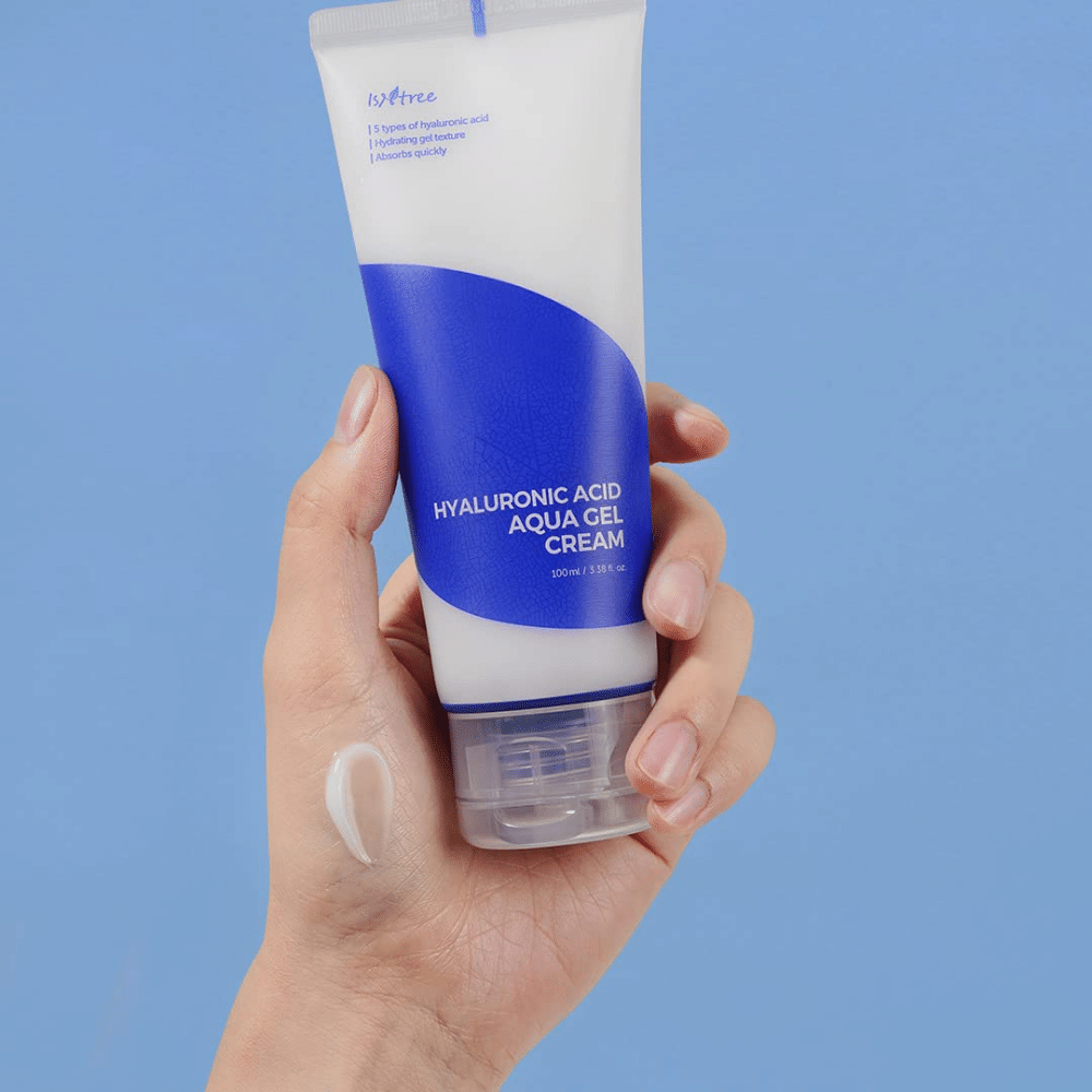 Ένα χέρι που κρατά έναν σωλήνα Isntree Hyaluronic Acid Aqua Gel Cream 100ml σε μπλε φόντο.